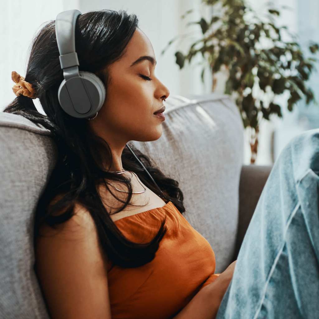 A woman with her eyes closed wearing headphones and sitting on the couch.