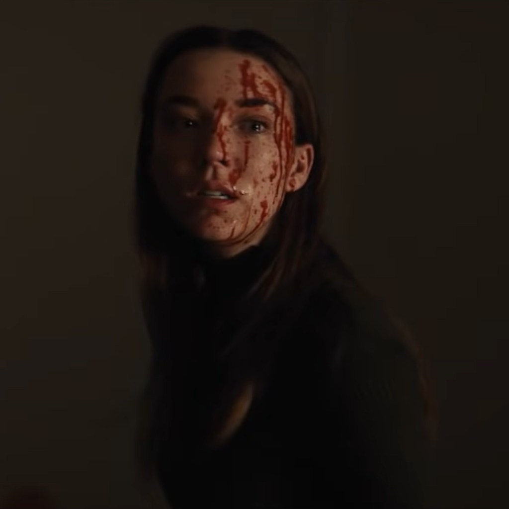 Nicole Brydon Bloom as Sarah, with a blood spatter on her face, in the horror movie Apartment 1BR.