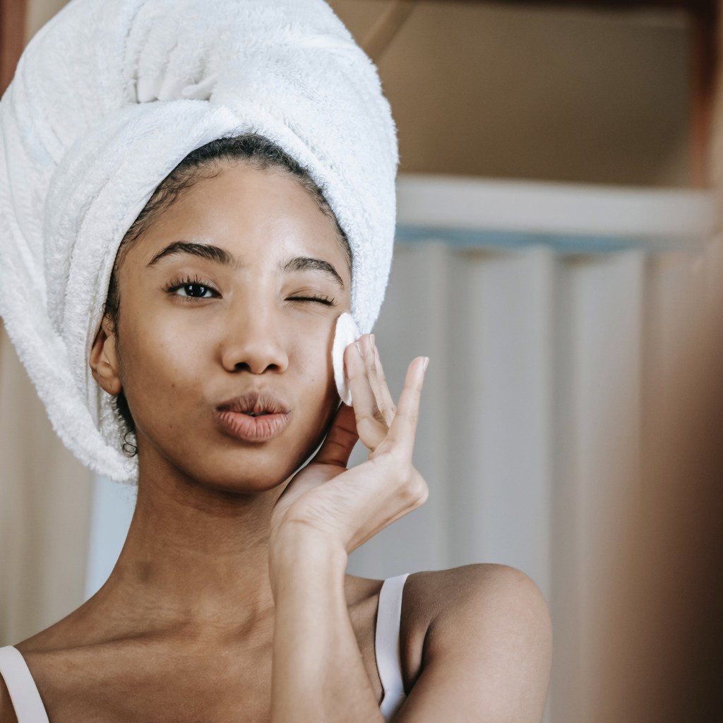 woman applying skincare with hair wrapped in towel