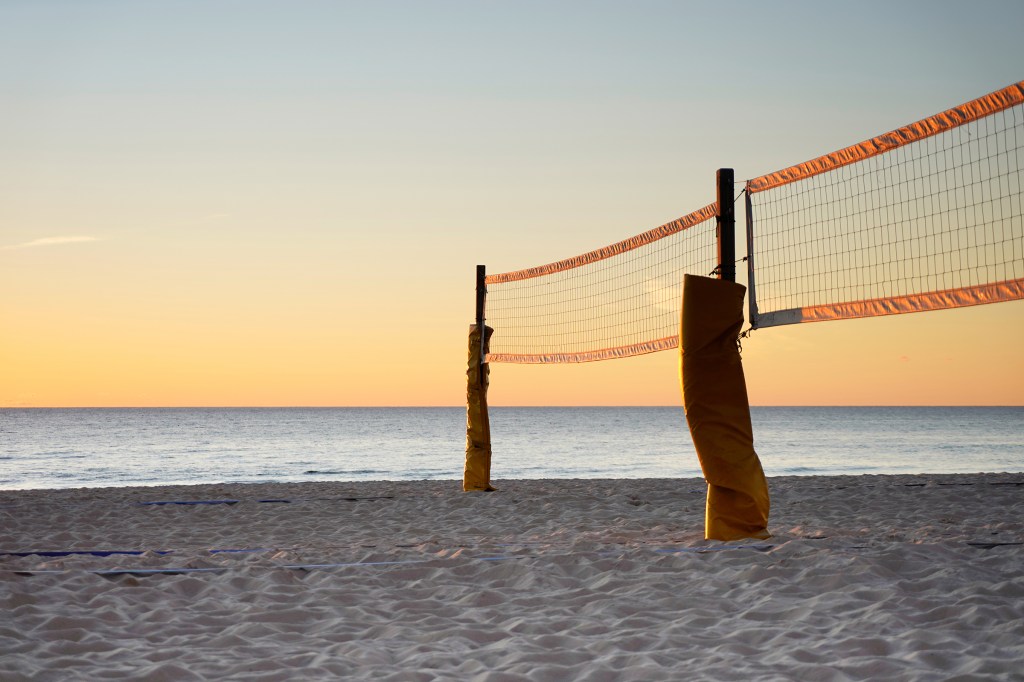 Beach volleyball net on beach during sunset. Beach volleyball is a team sport played by two teams of two or more players on a sand court divided by a net.